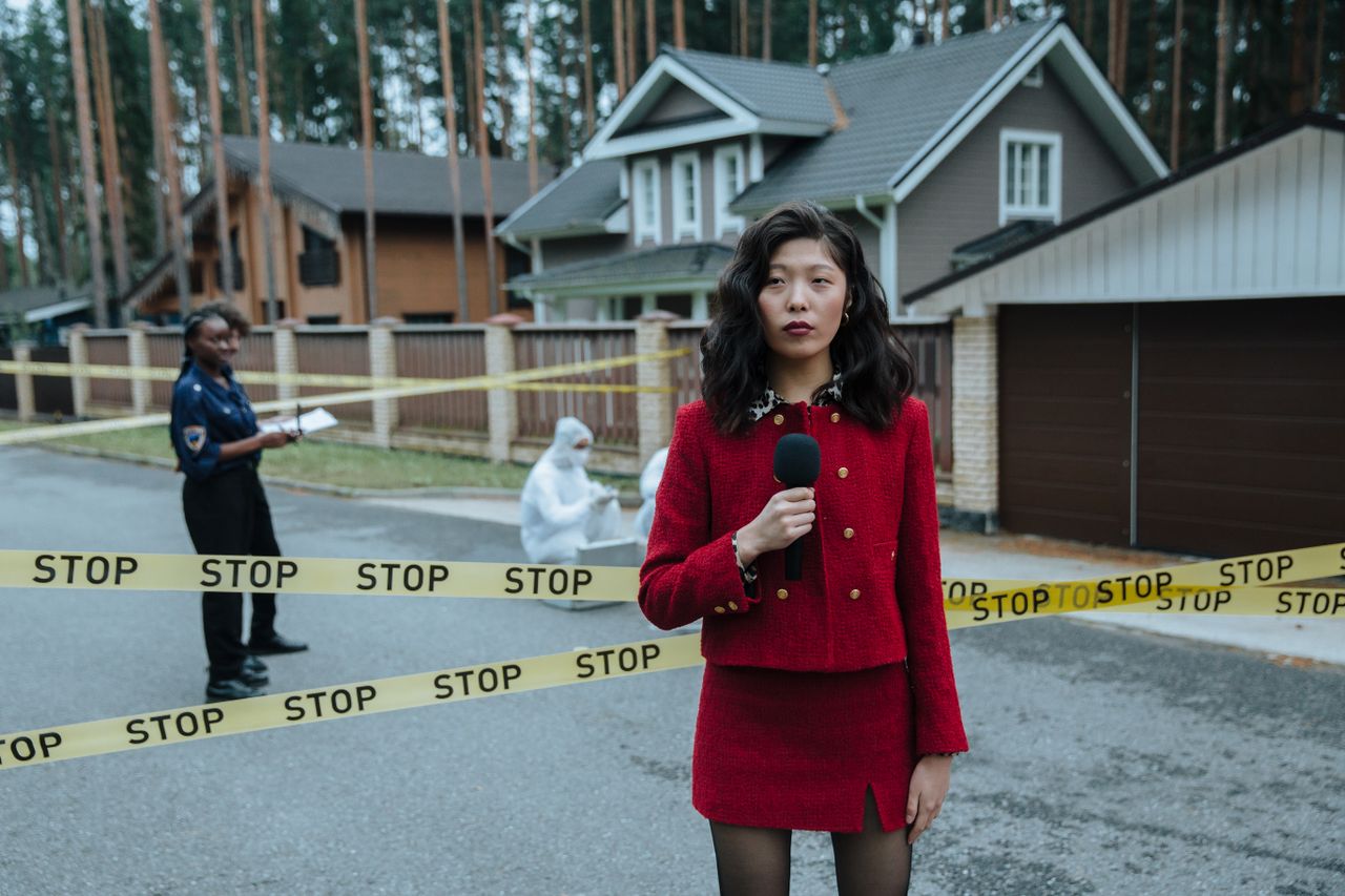 Crafting Captivating Headlines: Your awesome post title goes here A journalist in a red outfit reporting live from a crime scene outdoors with stop tape and police presence.