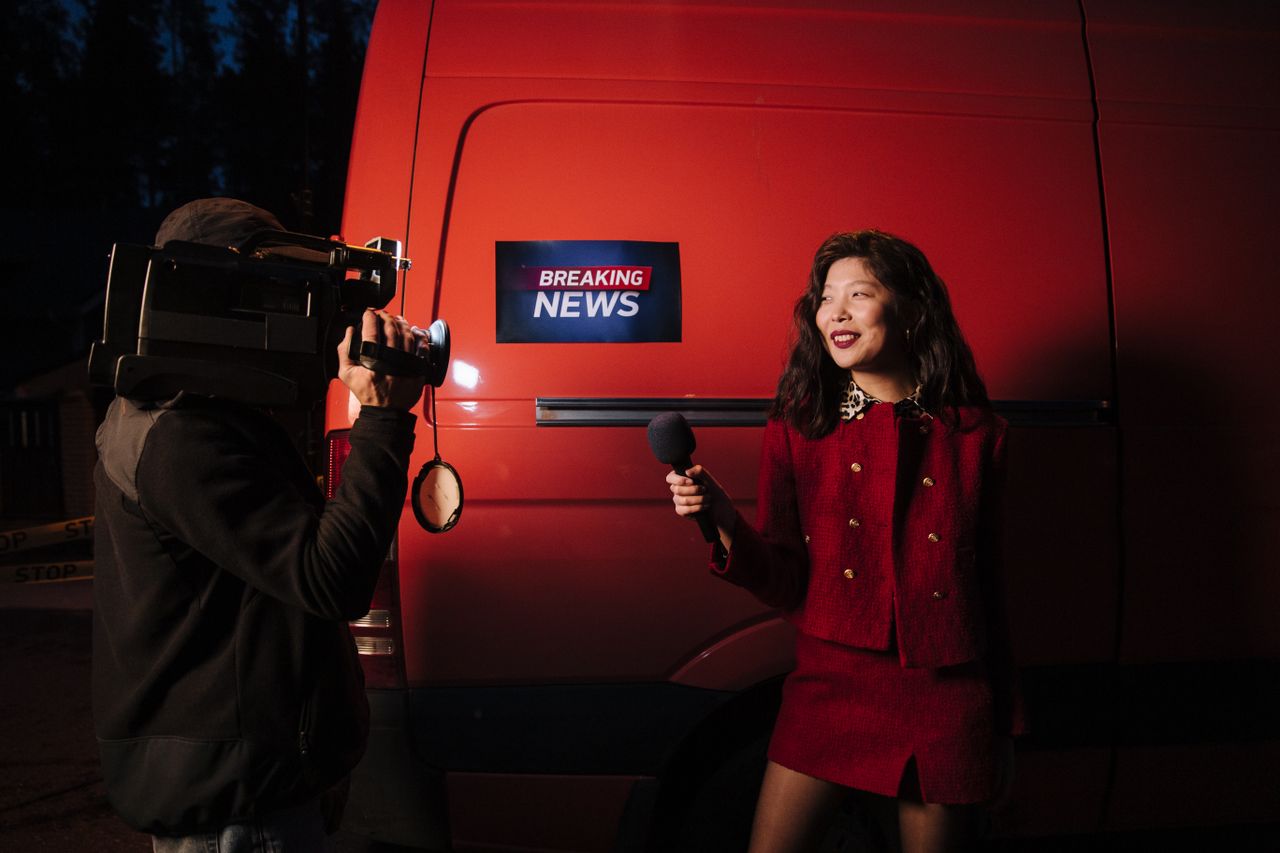 Services Dynamic news reporter holding microphone near red van during nighttime outdoor broadcast.