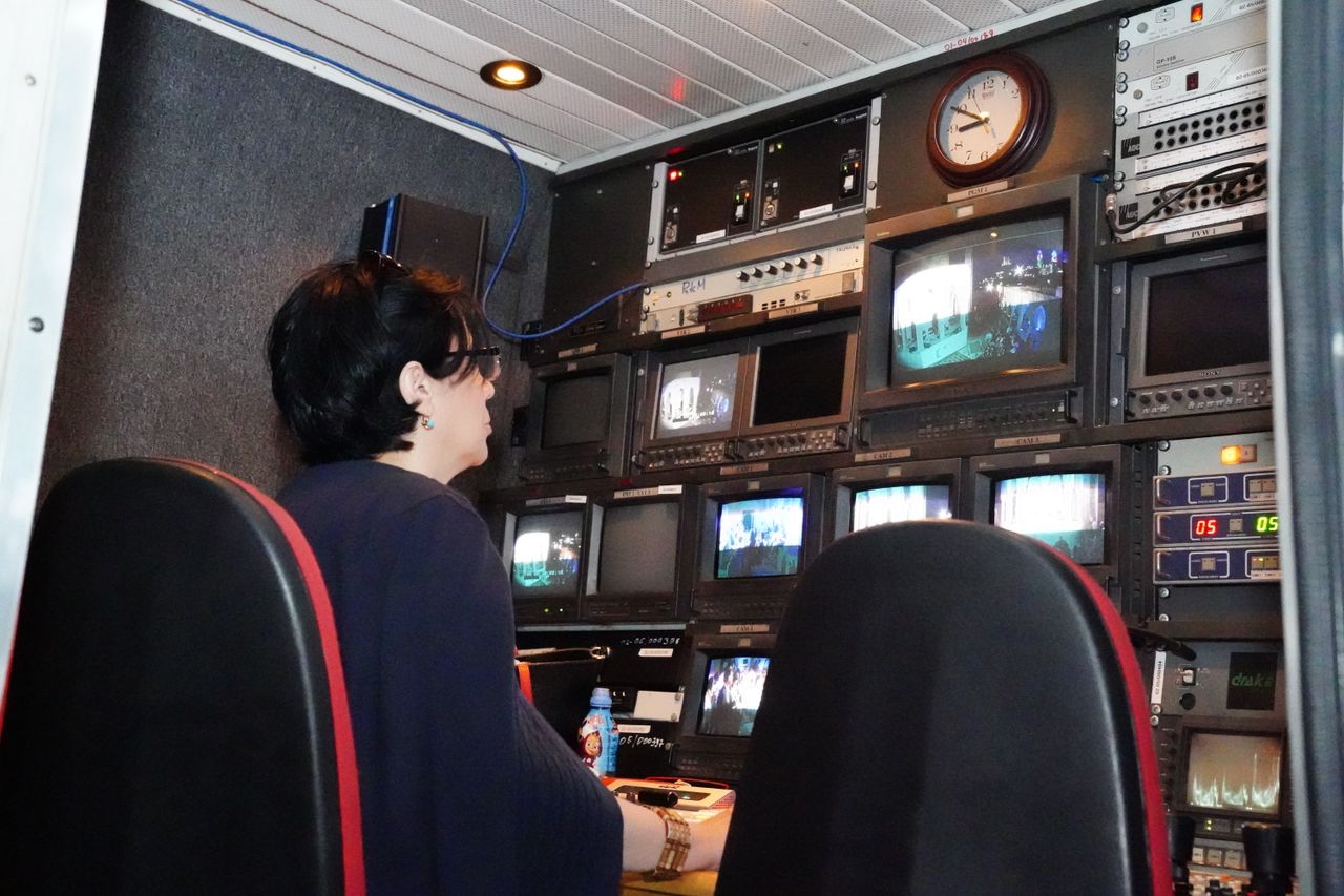 About A professional in a TV broadcast control room with multiple screens and equipment.